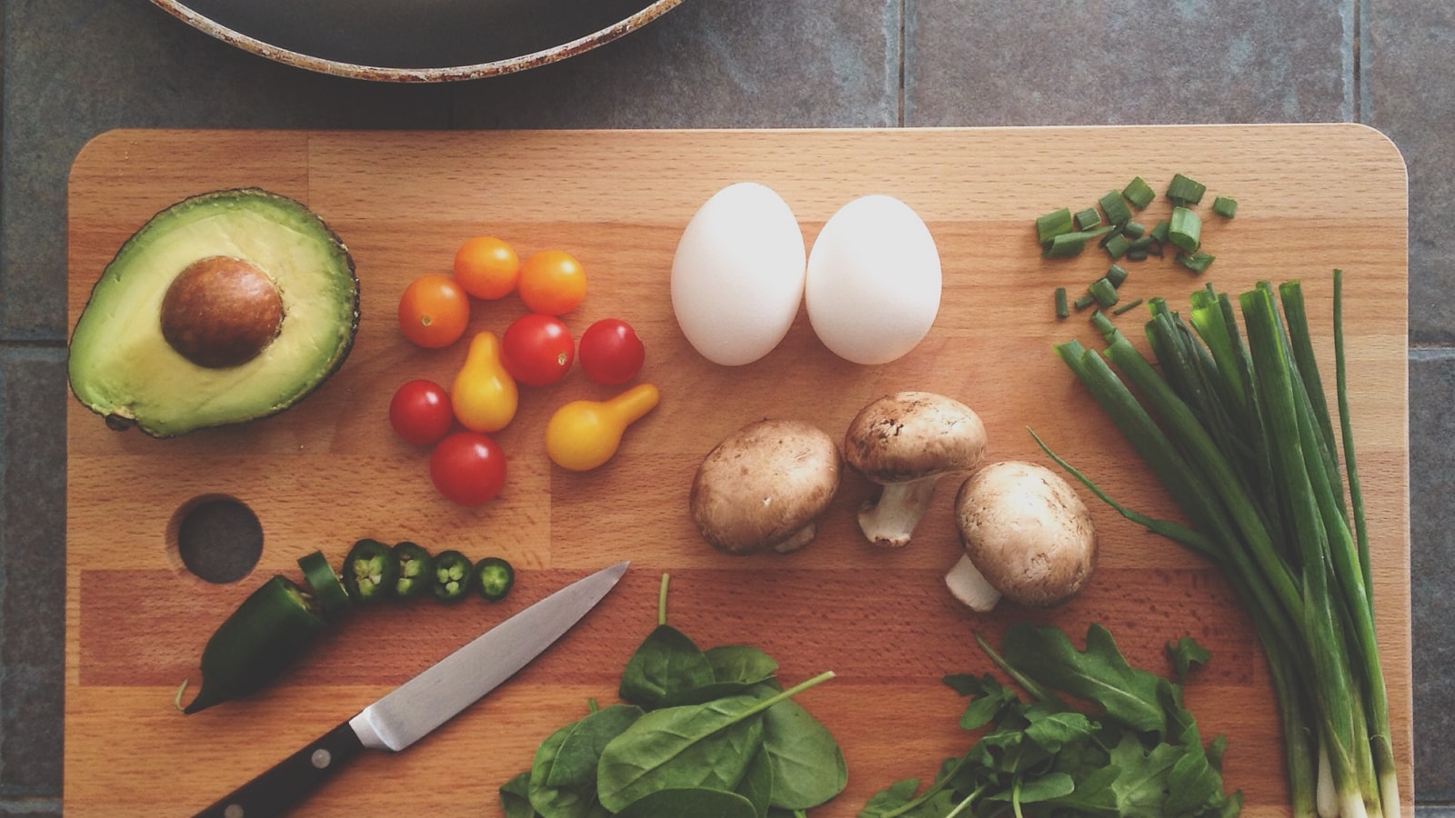 A notebook and pen beside fresh vegetables and a cup of coffee on a kitchen table.