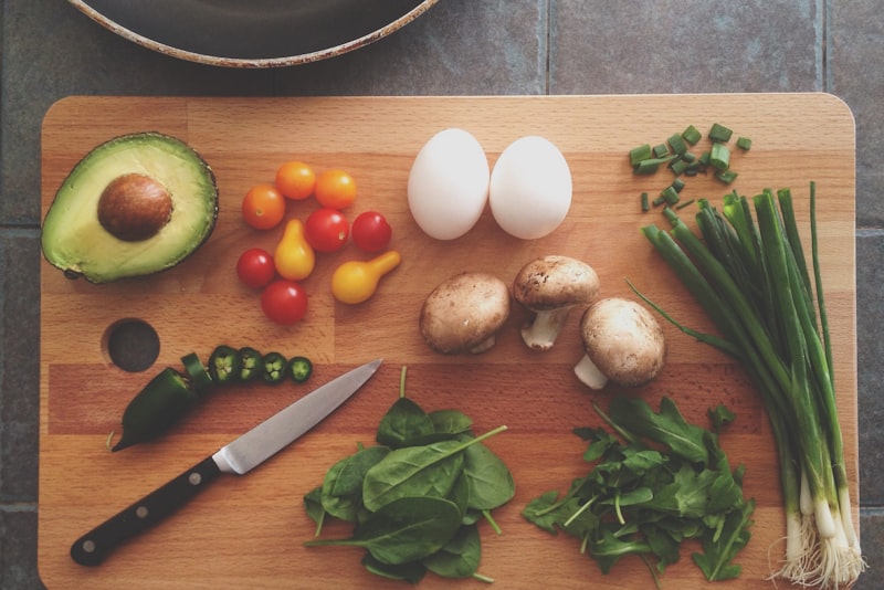 A notebook and pen beside fresh vegetables and a cup of coffee on a kitchen table.
