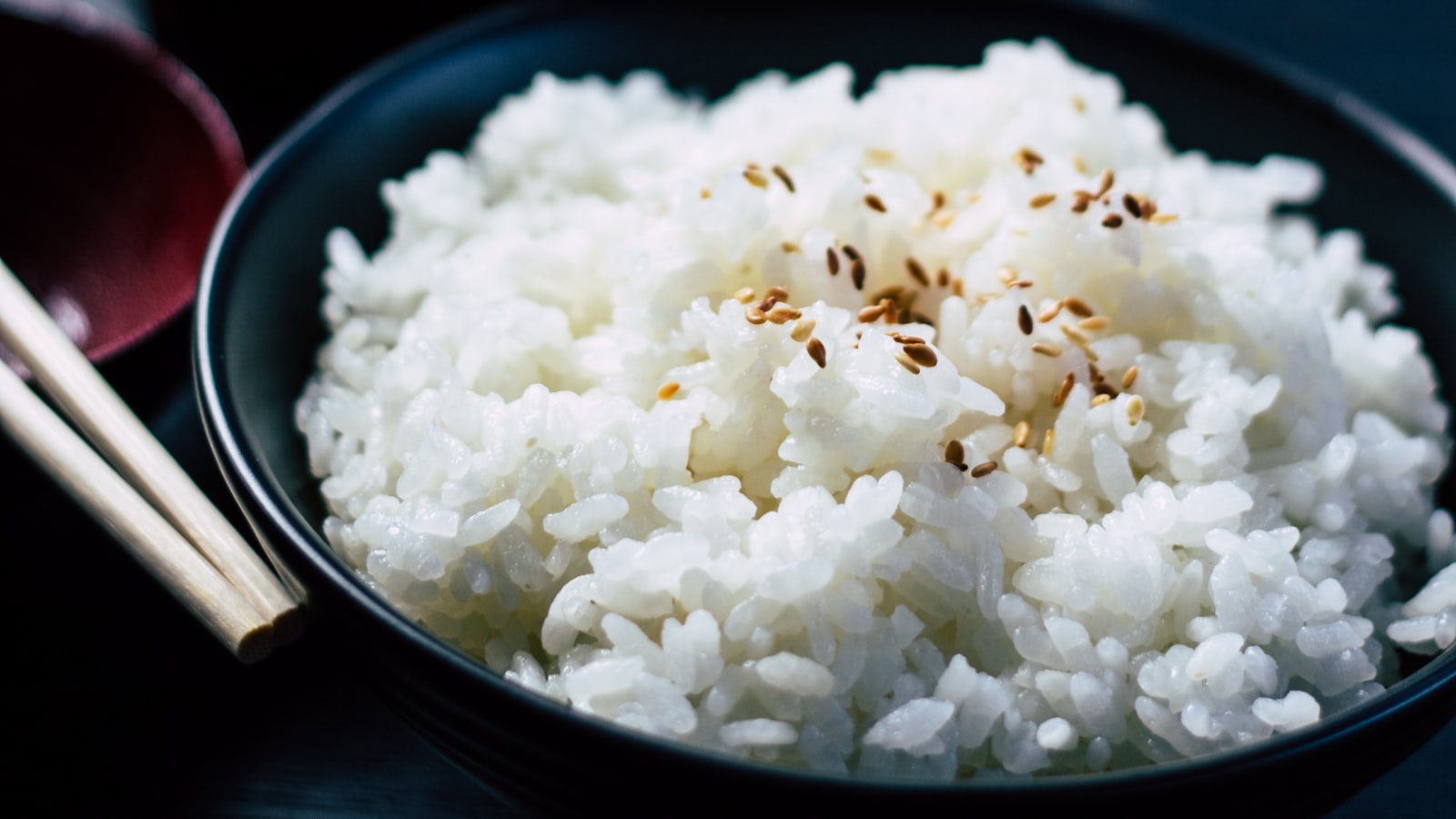 A bowl of fluffy cooked white rice with a pair of wooden chopsticks resting on top.