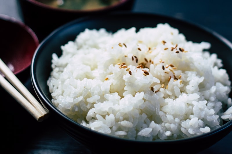 A bowl of fluffy cooked white rice with a pair of wooden chopsticks resting on top.