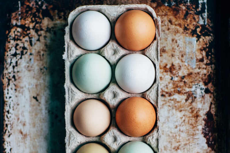 A cardboard carton holding a dozen eggs in shades of white, brown, and pale blue-green.