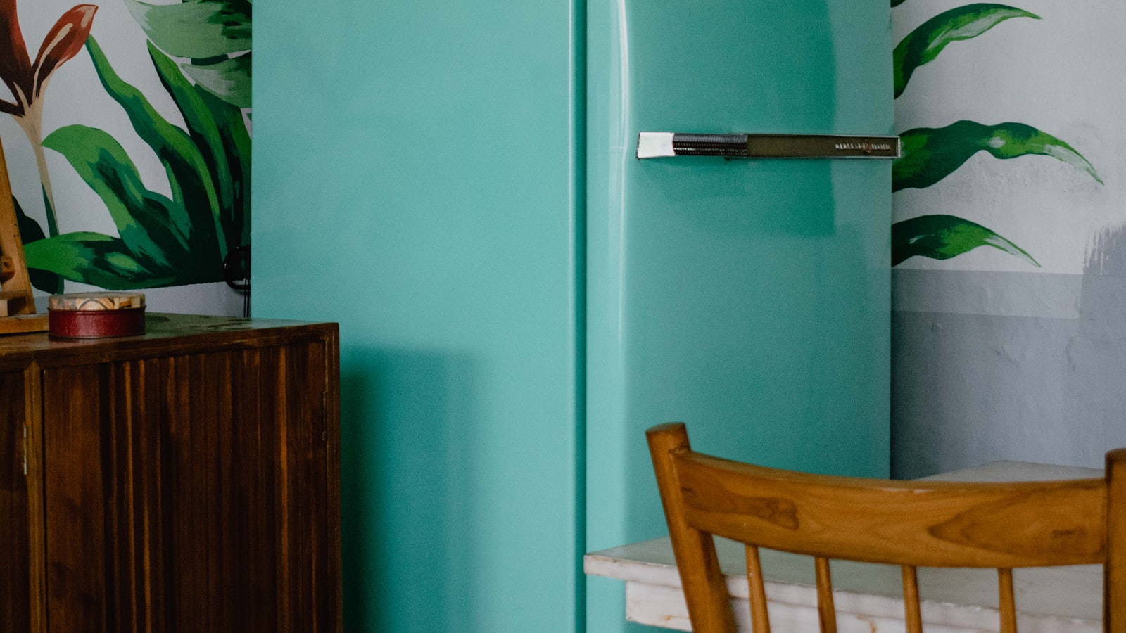A pale teal vintage refrigerator standing in a kitchen corner beside a wooden chair.