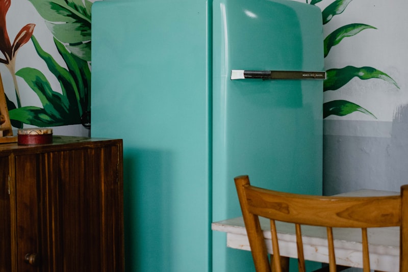 A pale teal vintage refrigerator standing in a kitchen corner beside a wooden chair.
